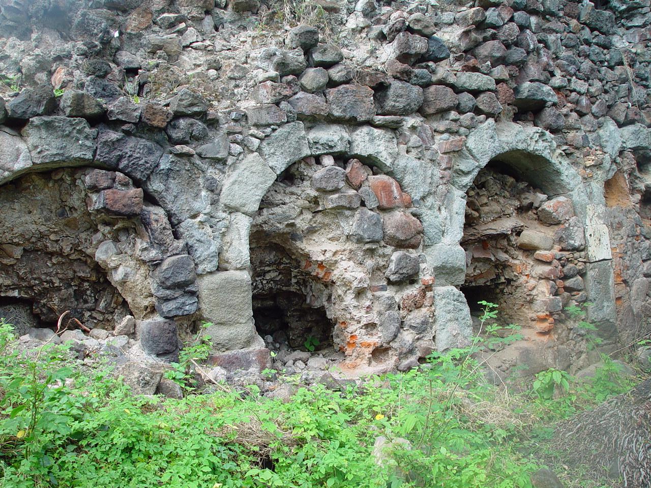 Mur de la sucrerie percé d'une série d'ouvertures en arc, encadrées de pierres de taille et partiellement comblées de blocs et de briques réfractaires rougies par le feu.
